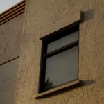 Fenêtre projetant une ombre sur un mur en stuc. Pensez films solaires bâtiment résidentiel Vaud.