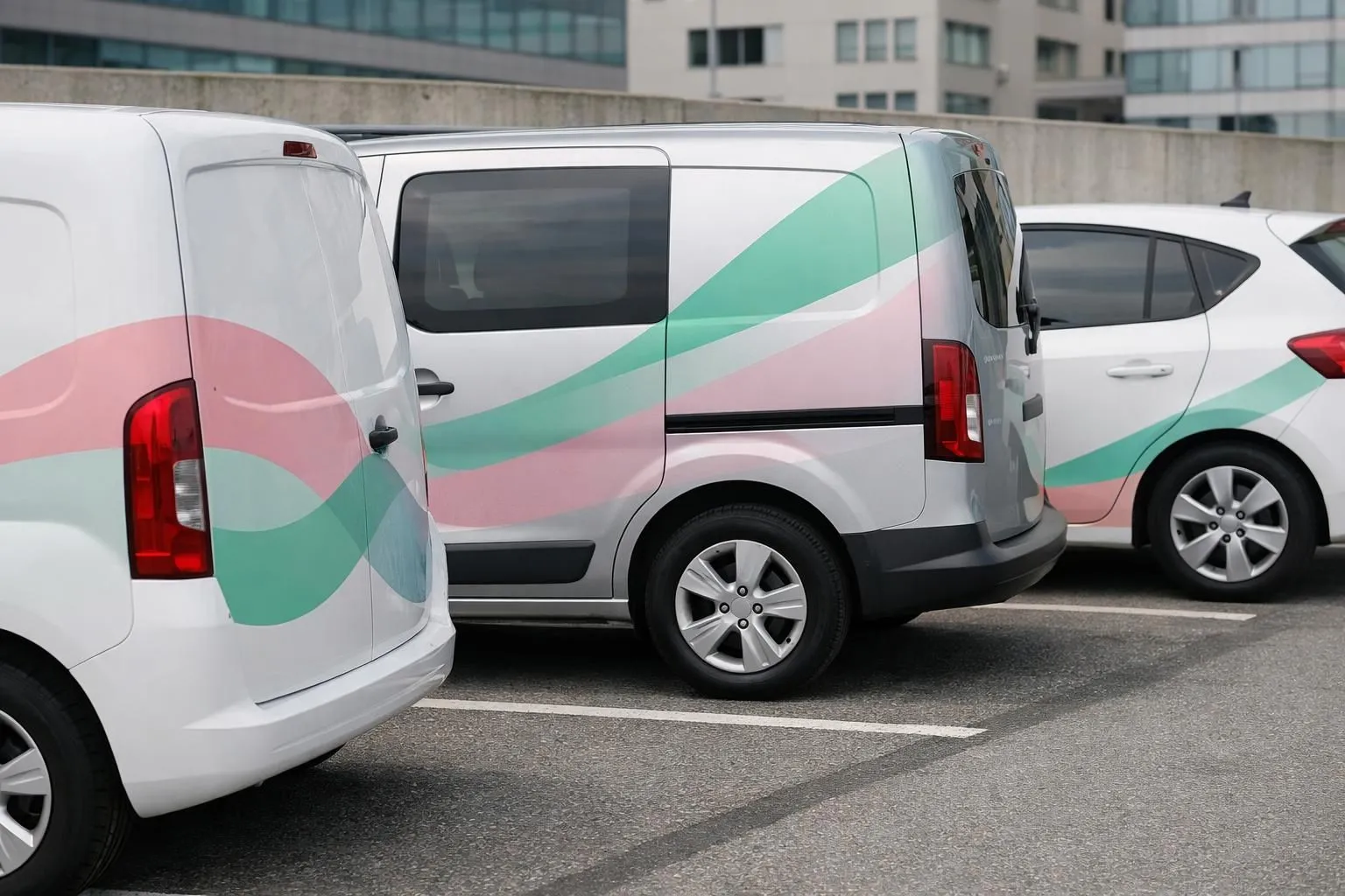 Five different commercial vehicles parked side by side displaying various vehicle branding techniques including full wraps, partial graphics, window decals, and magnetic signs on white delivery vans in Swiss urban parking area