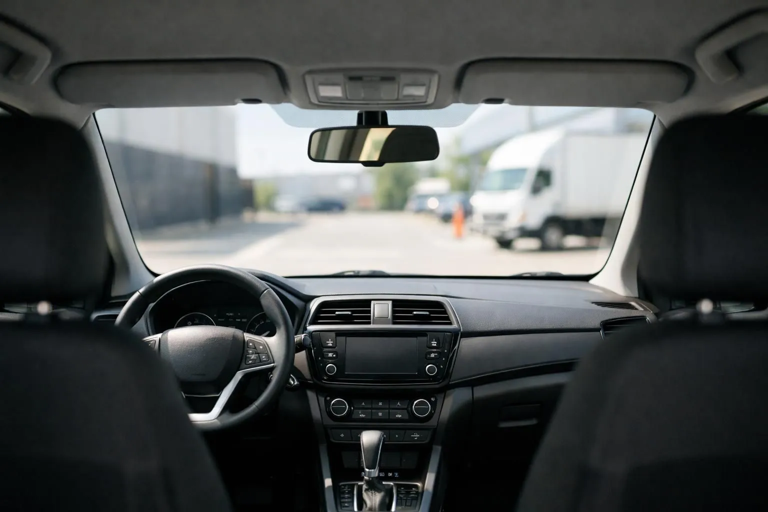 Car interior photograph showing clear contrast between transparent front windshield and darker rear windows, with dashboard visible and natural daylight streaming through, emphasizing visibility differences for driver safety in professional vehicle context