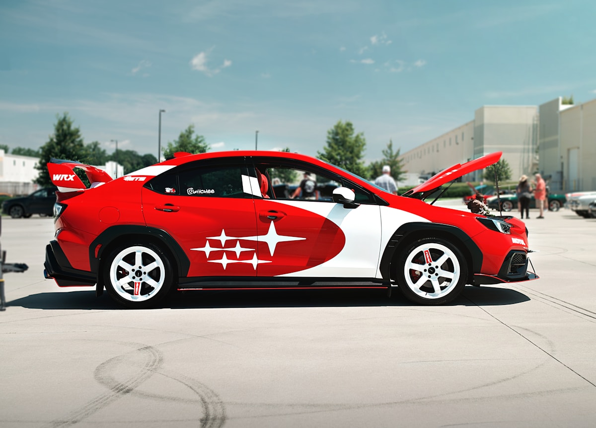 A red and white subaru at an outdoor car show.