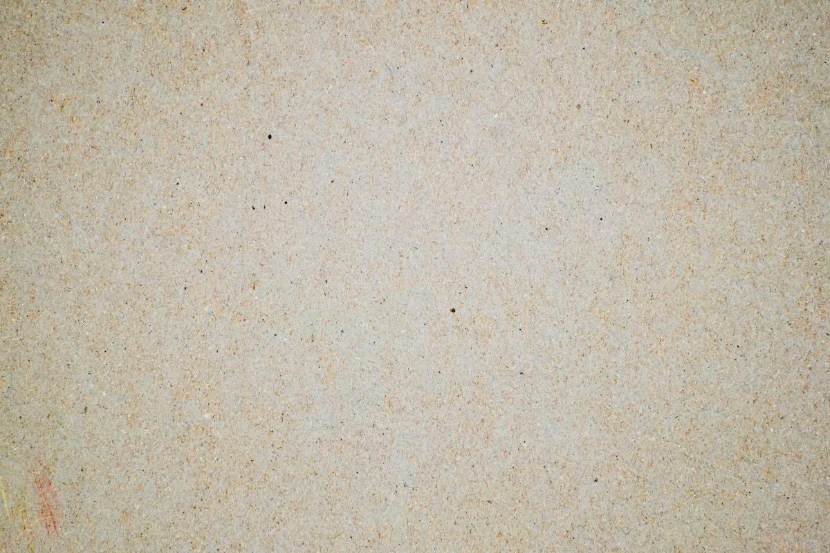 Texture granuleuse beige clair avec des taches sombres.