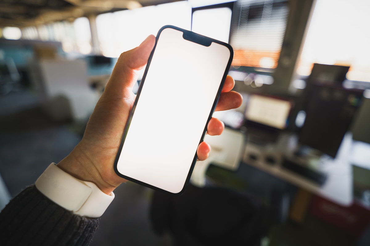 Smartphone à écran blanc tenu dans une main.
