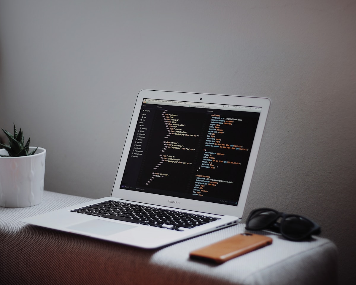 Ordinateur portable avec code de programmation à l'écran, sur un bureau avec une plante et des lunettes.