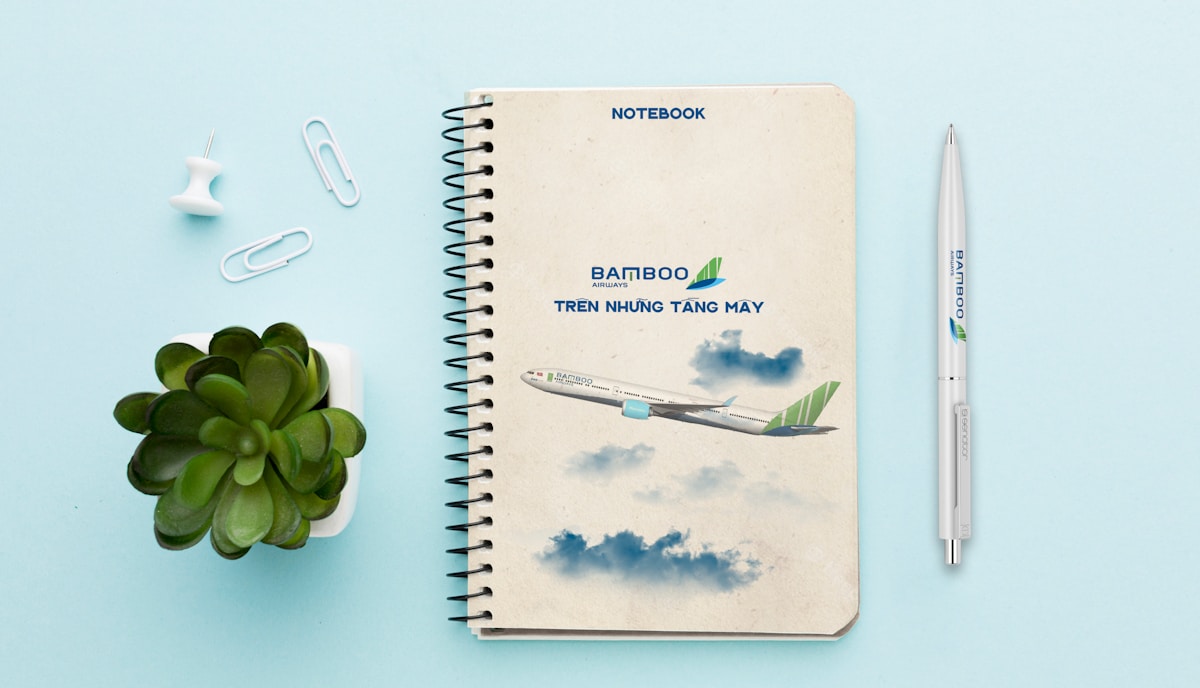 Cahier de notes avec logo de compagnie aérienne, stylo, plante verte et trombones.