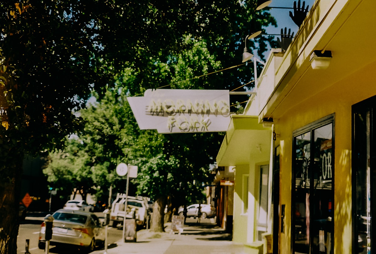 Rue animée avec commerces, arbres et enseigne de magasin.