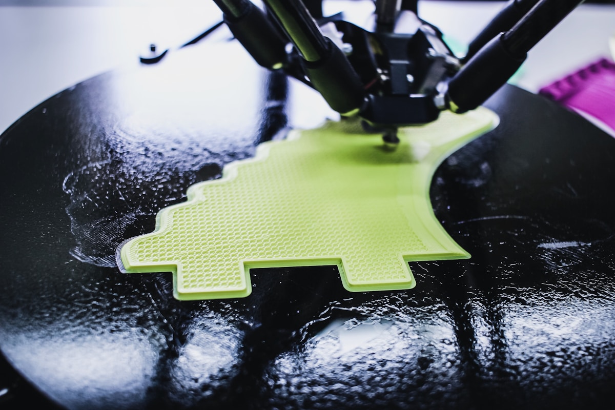 Imprimante 3D en action, extrudant un matériau vert sur une surface noire.