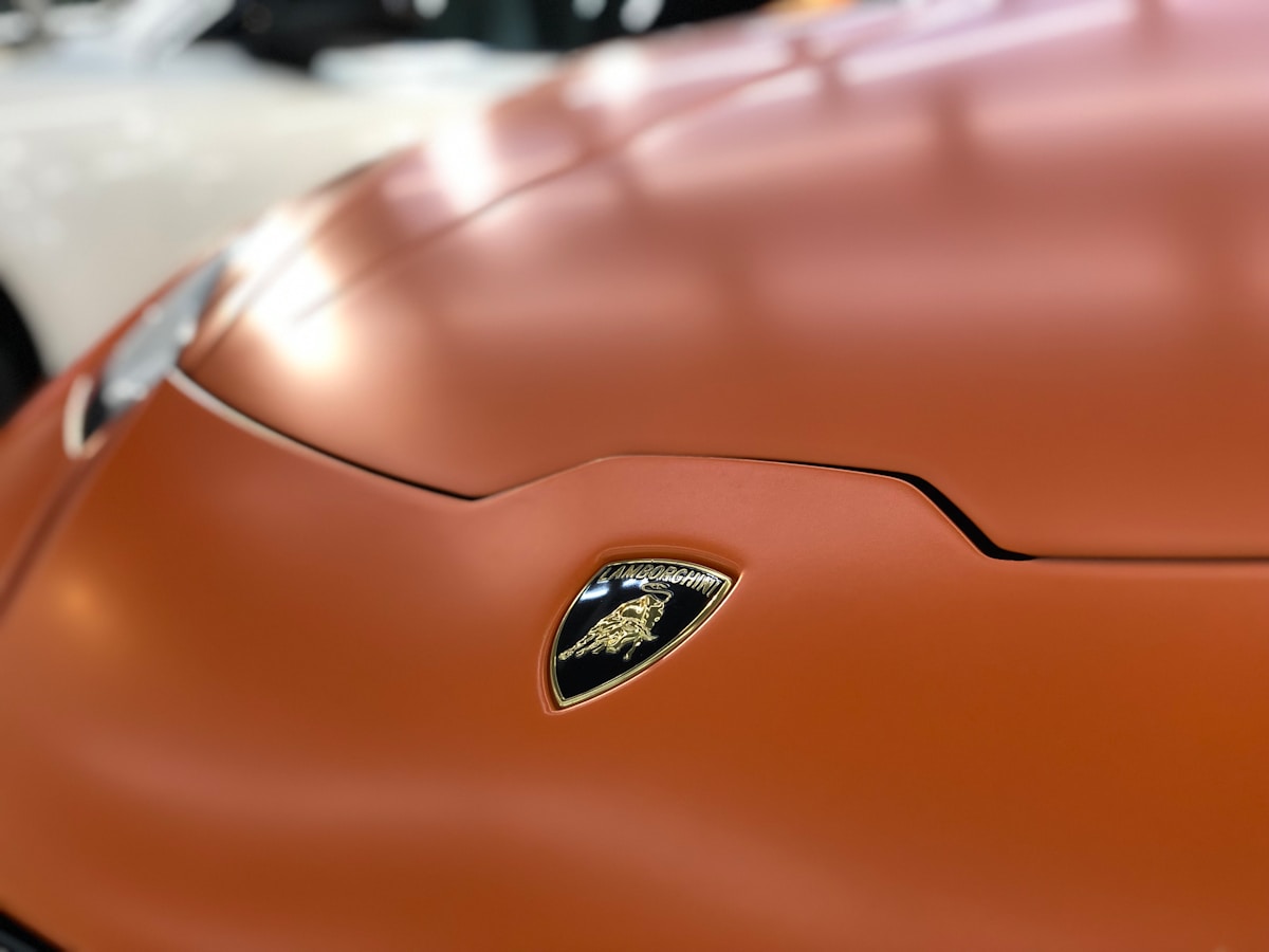Voiture de sport orange avec logo Lamborghini doré.