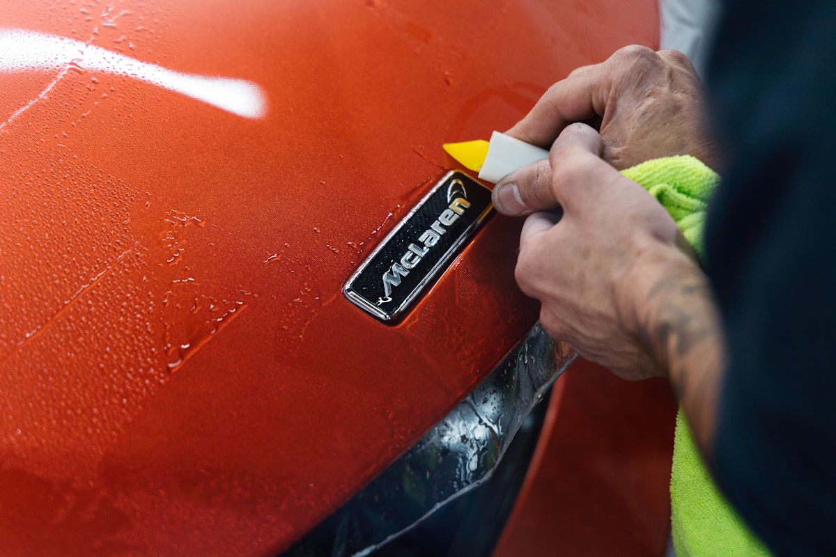 Mains appliquant un produit de nettoyage sur une surface orange brillante.