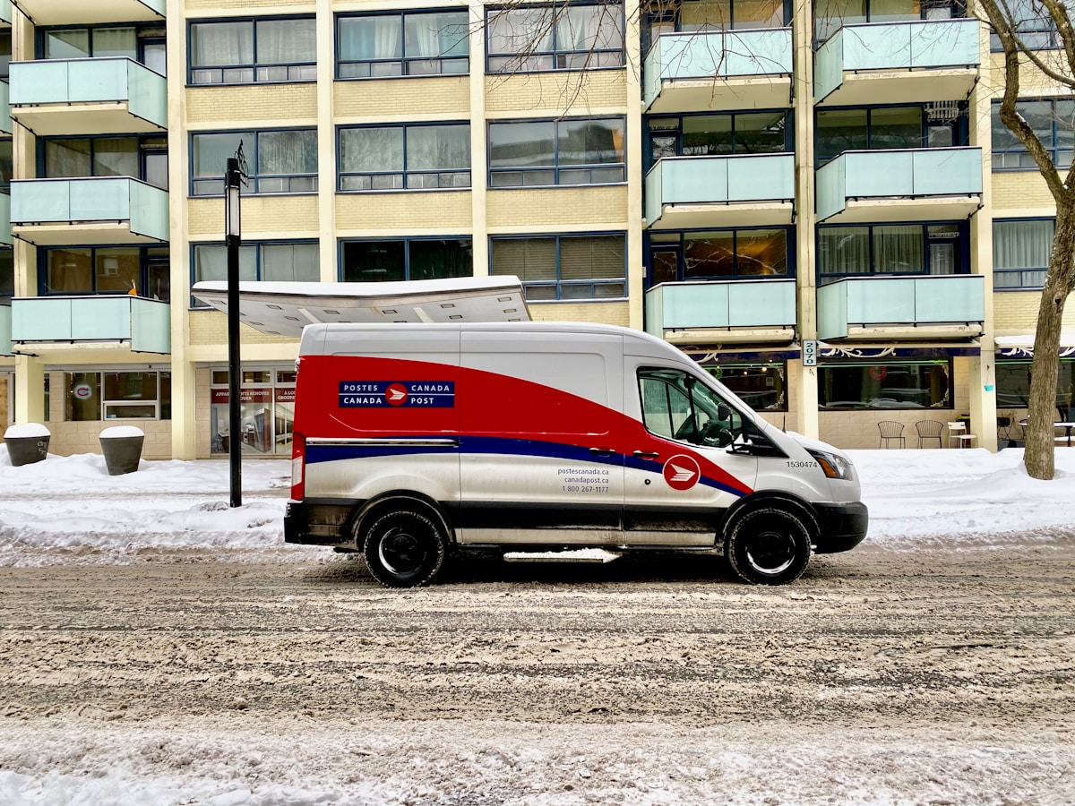 Camionnette de livraison des Postes canadiennes dans un environnement urbain enneigé.