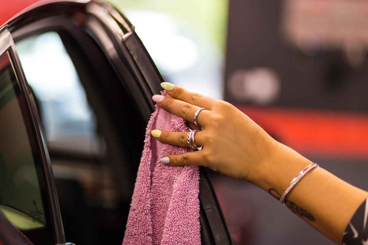 Mains féminines tenant un chiffon rose pour nettoyer une fenêtre de voiture.