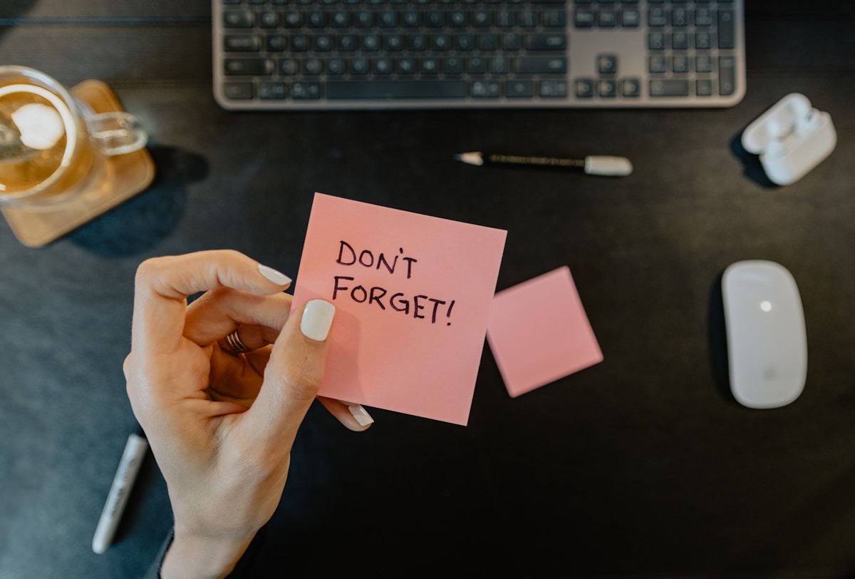 Main tenant un post-it rose avec le texte "Don't forget!"