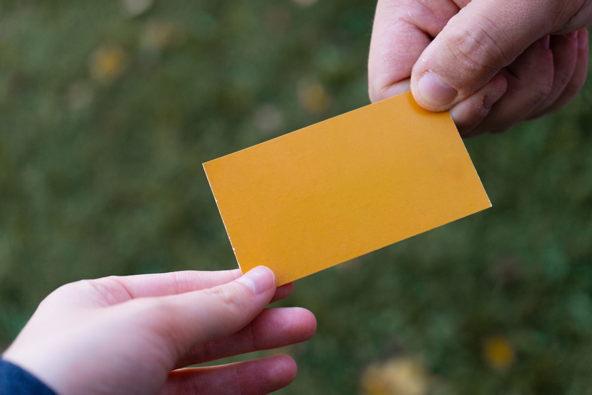 Carte de visite jaune tenue dans des mains.