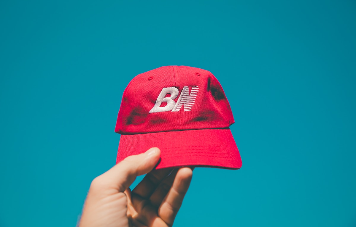 Casquette rouge avec logo BX sur fond bleu turquoise.