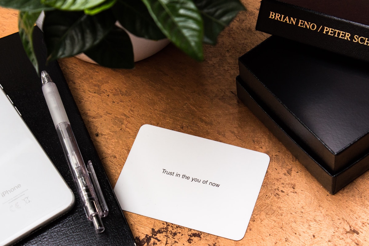 Livres, stylo, carte avec message, téléphone, plante verte sur un bureau en bois.
