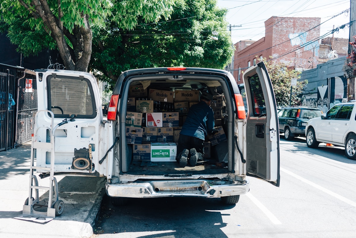 Camionnette blanche remplie de boîtes de bière Corona sur une rue urbaine.