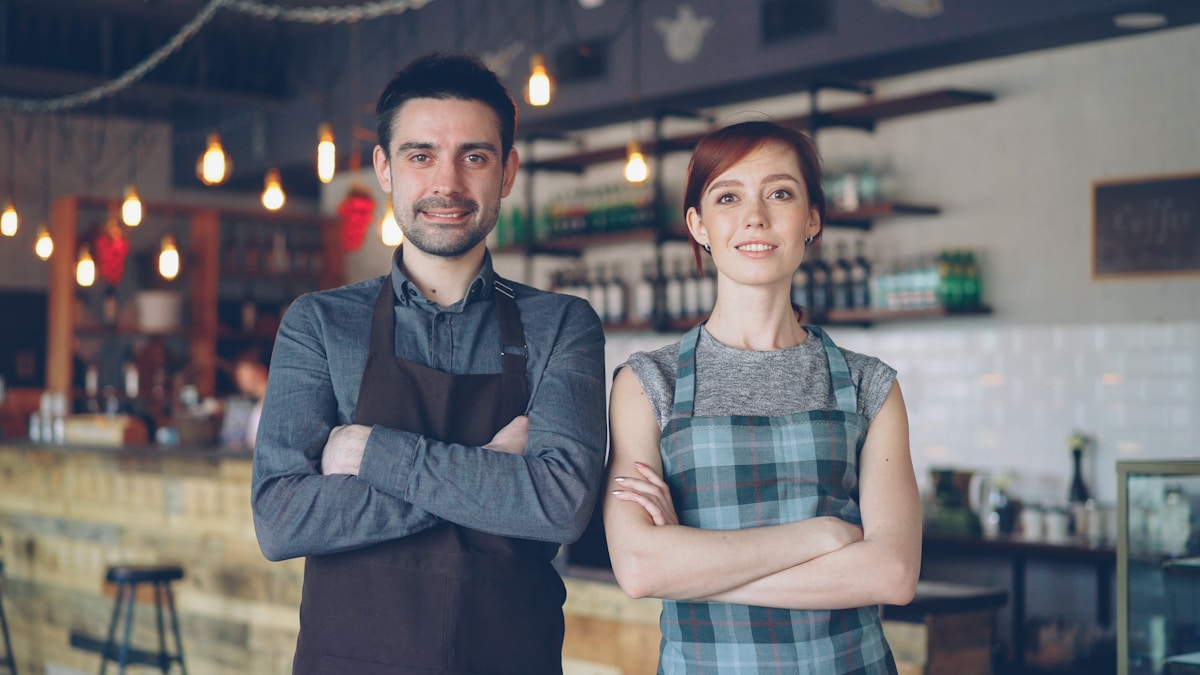 Deux employés souriants d'un café, debout côte à côte.