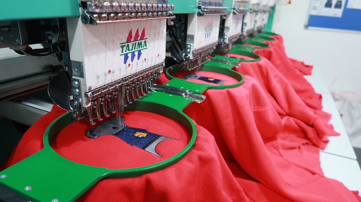 Machines de broderie industrielles avec motifs colorés sur tissus rouges.