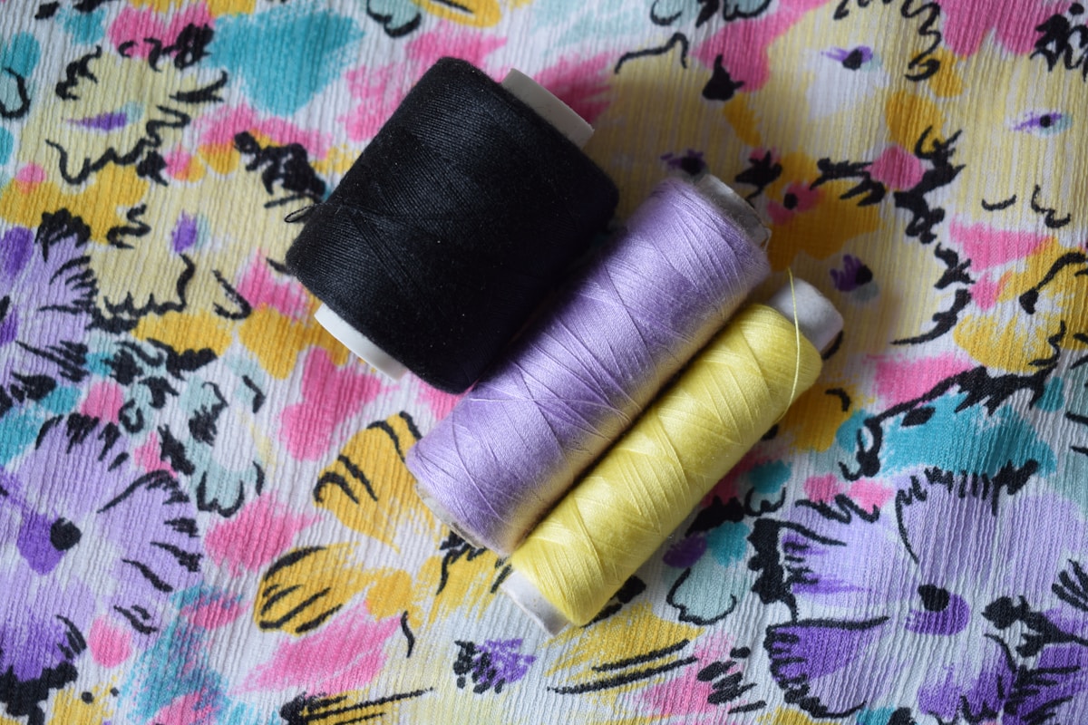 Bobines de fil de couleurs vives sur un motif floral abstrait.