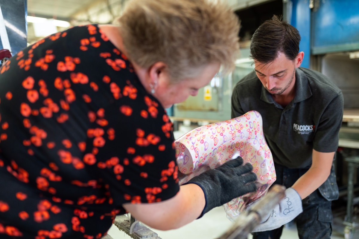 Deux personnes travaillant ensemble dans un atelier, l'un enveloppant un objet dans un papier motif floral.