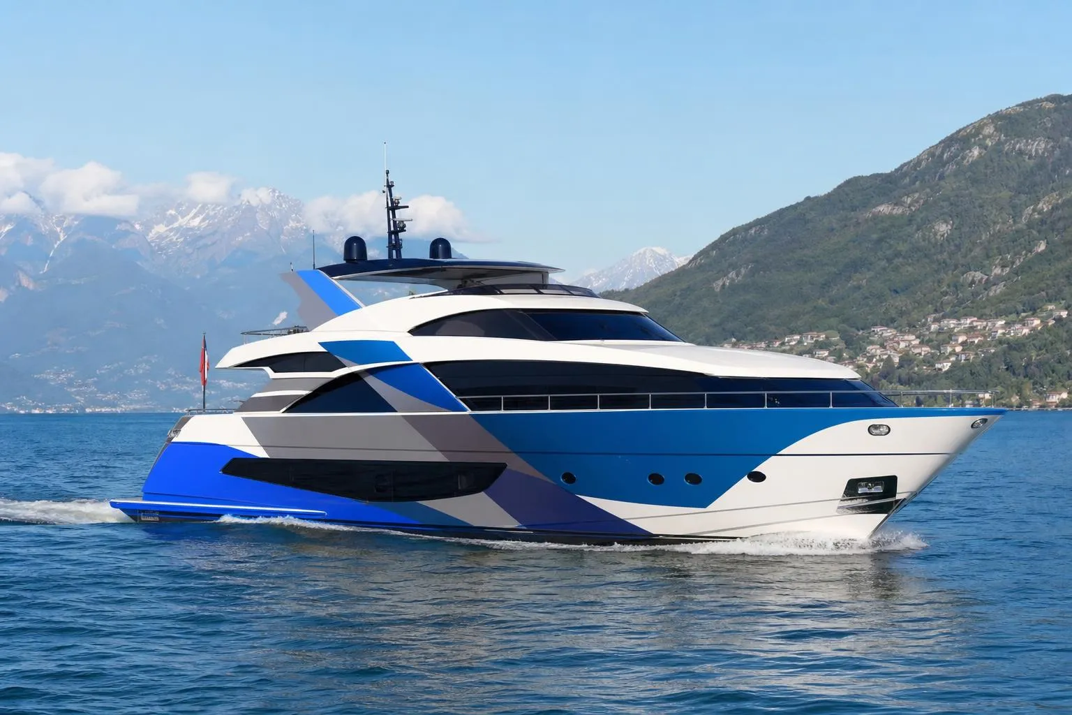 Yacht de luxe bleu et blanc naviguant sur l'eau avec des montagnes en arrière-plan.