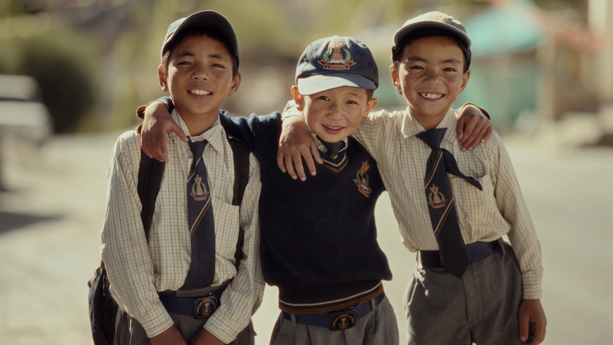 Trois jeunes garçons souriants en uniforme scolaire.