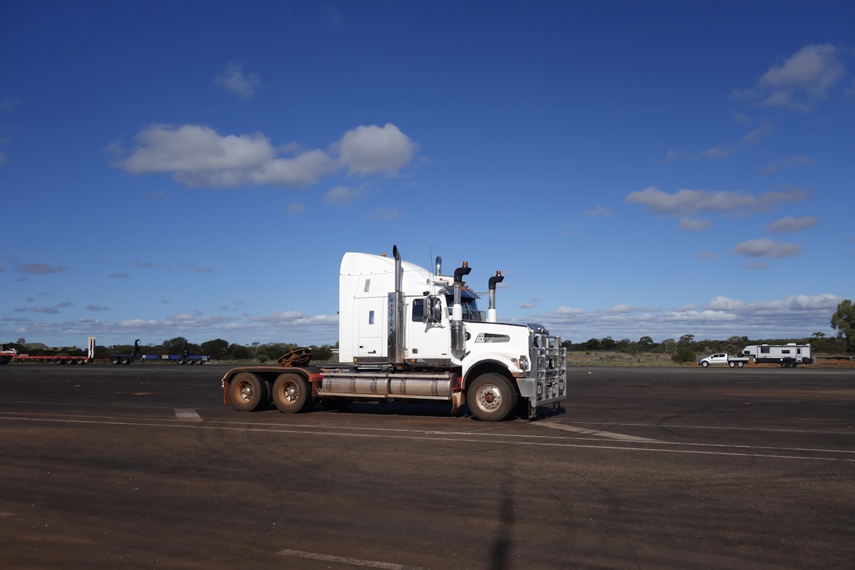 Camion semi-remorque blanc sur une route déserte sous un ciel bleu.