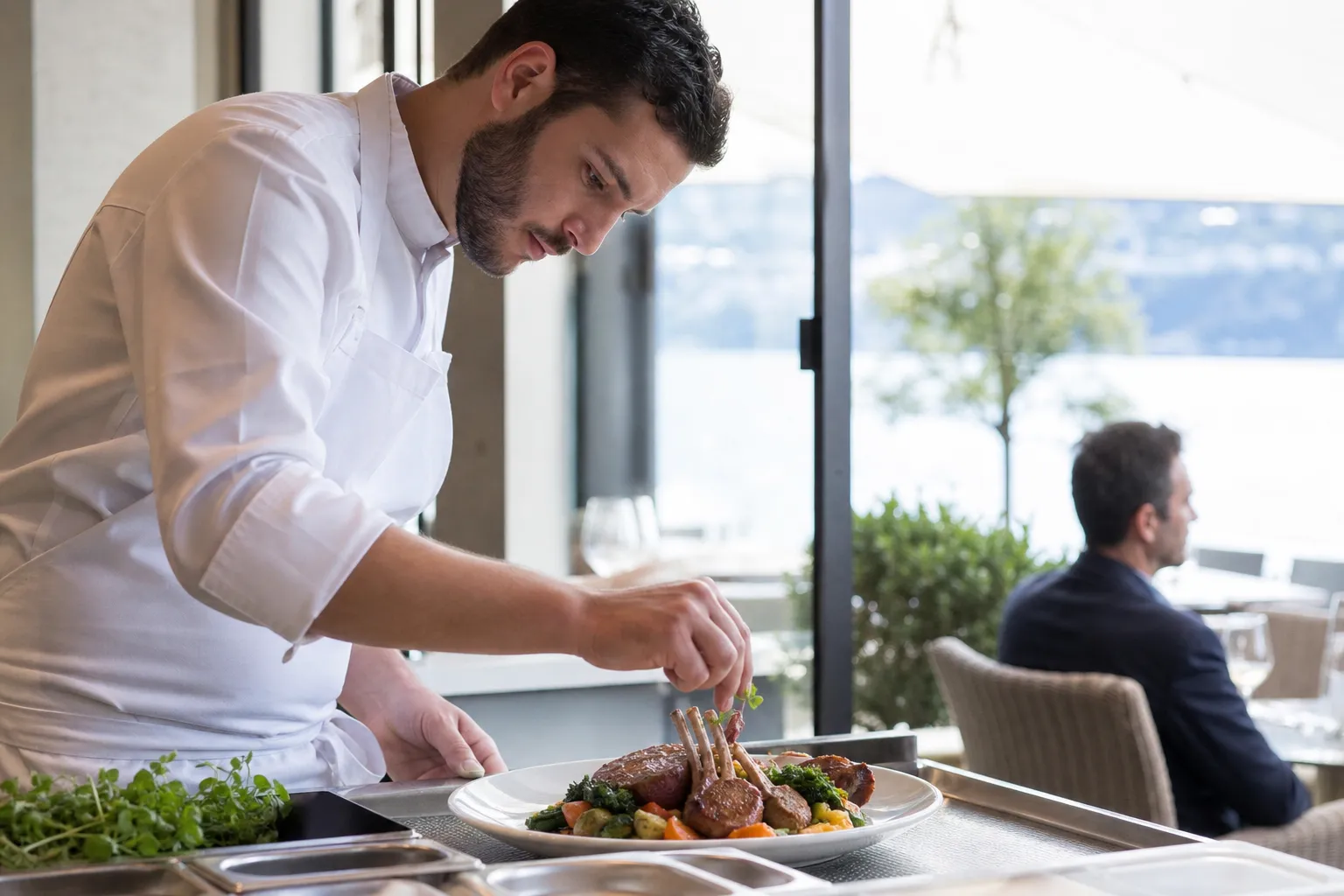 Chef préparant un plat d'agneau grillé dans un restaurant à Lausanne, lumière naturelle et ambiance chaleureuse.