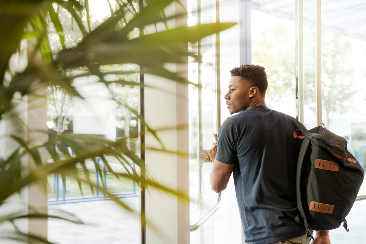 Jeune homme noir avec sac à dos ouvrant une porte vitrée