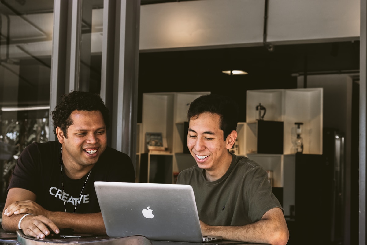 Deux hommes souriants travaillant ensemble sur un ordinateur portable.