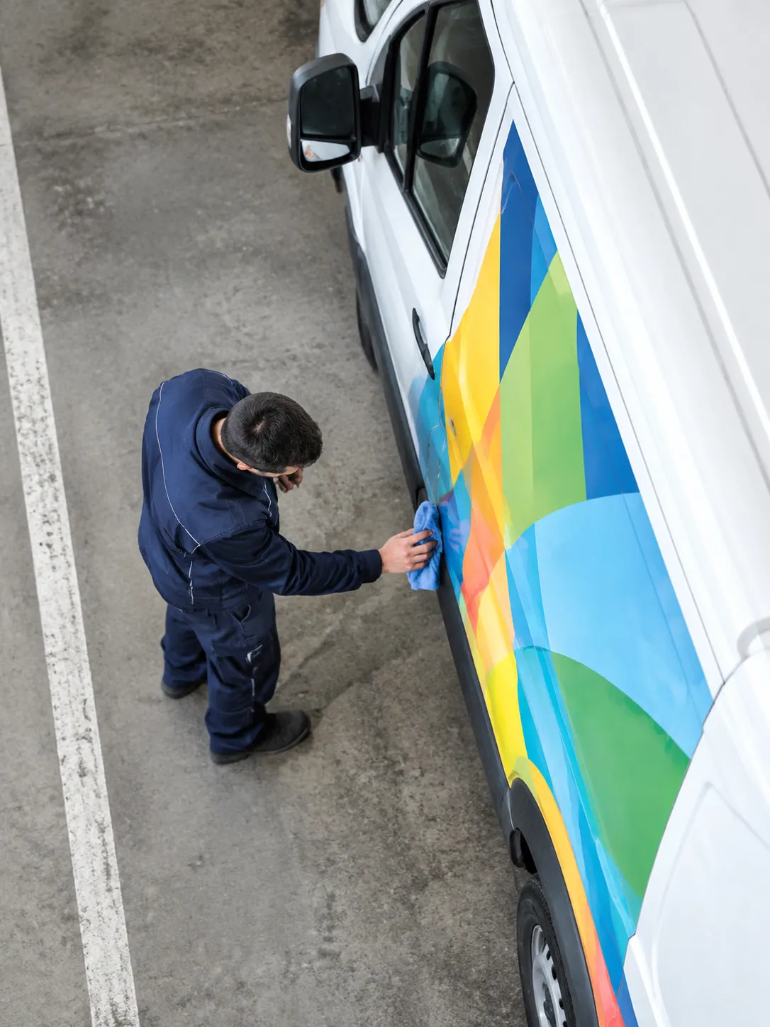 Homme nettoyant une camionnette blanche aux motifs colorés.