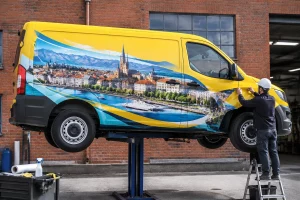 Camion utilitaire original avec covering créatif suspendu devant mur d'atelier à Lausanne, lumière naturelle, conducteur ajus