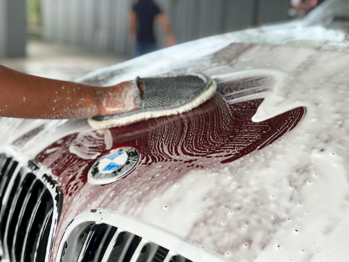 Main savonné avec gant nettoyant, capot BMW rouge en lavage.