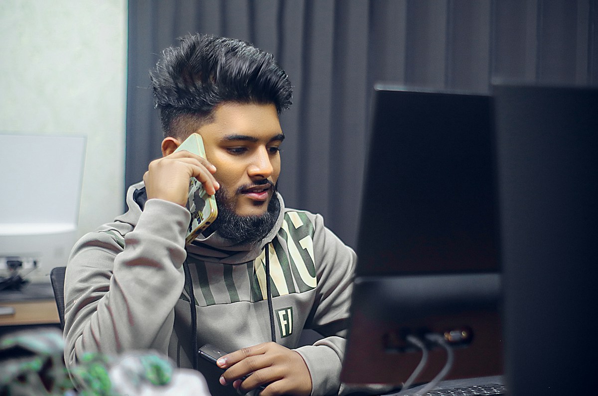 Homme barbu au téléphone devant un ordinateur portable.