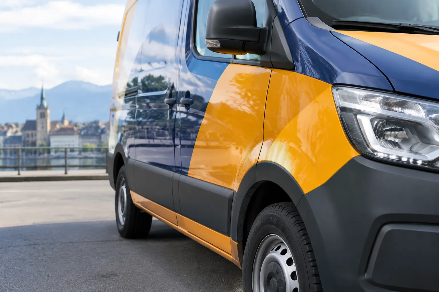 Camionnette orange et bleue devant un paysage urbain alpin